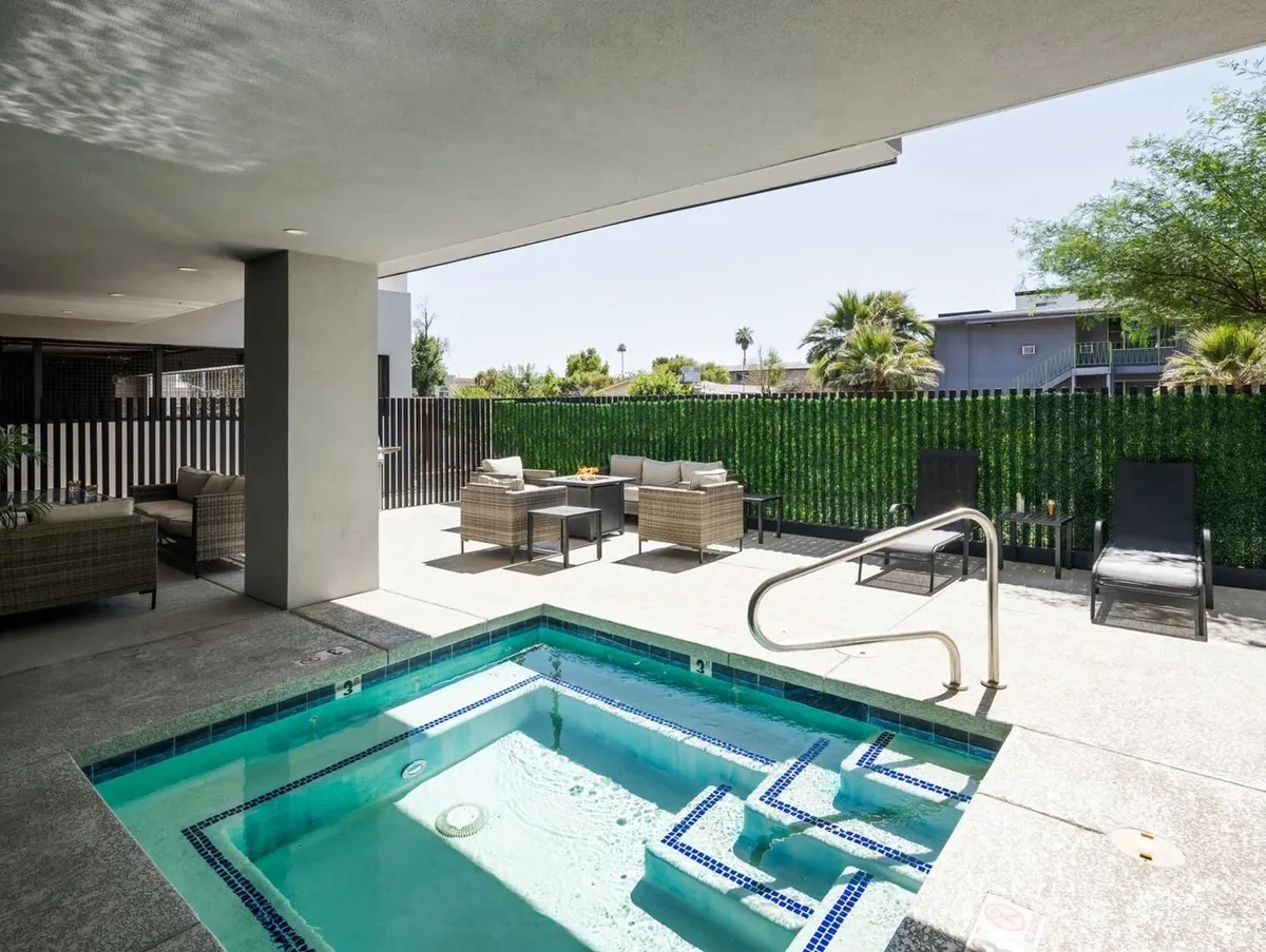 An inviting outdoor hot tub area framed by landscaped greenery and adjacent seating. The jacuzzi is the focal point, promising relaxation, while nearby seating hints at group gatherings under the sun or stars.