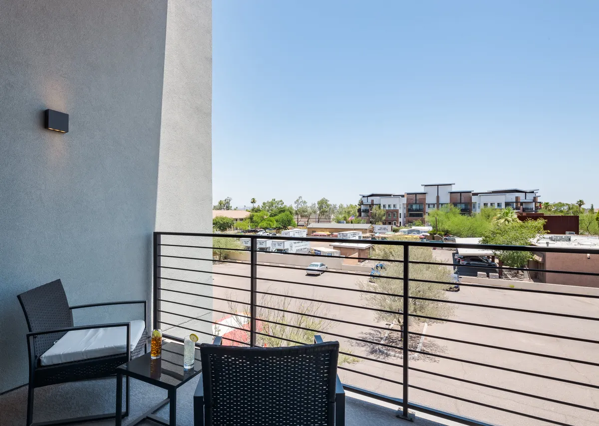 An exterior view of a private balcony with cozy seating and a scenic outlook over the surrounding area. The tranquil atmosphere is perfect for quiet retreats, morning coffee, or reading a book in solitude, showcasing the property's blend of privacy and connection to the outdoors.