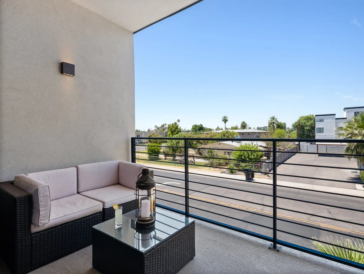 A serene balcony with outdoor seating and a glass table, overlooking the surrounding neighborhood. The balcony is an extension of the indoor living space, providing a perfect spot for enjoying morning coffee or evening cocktails with a view.