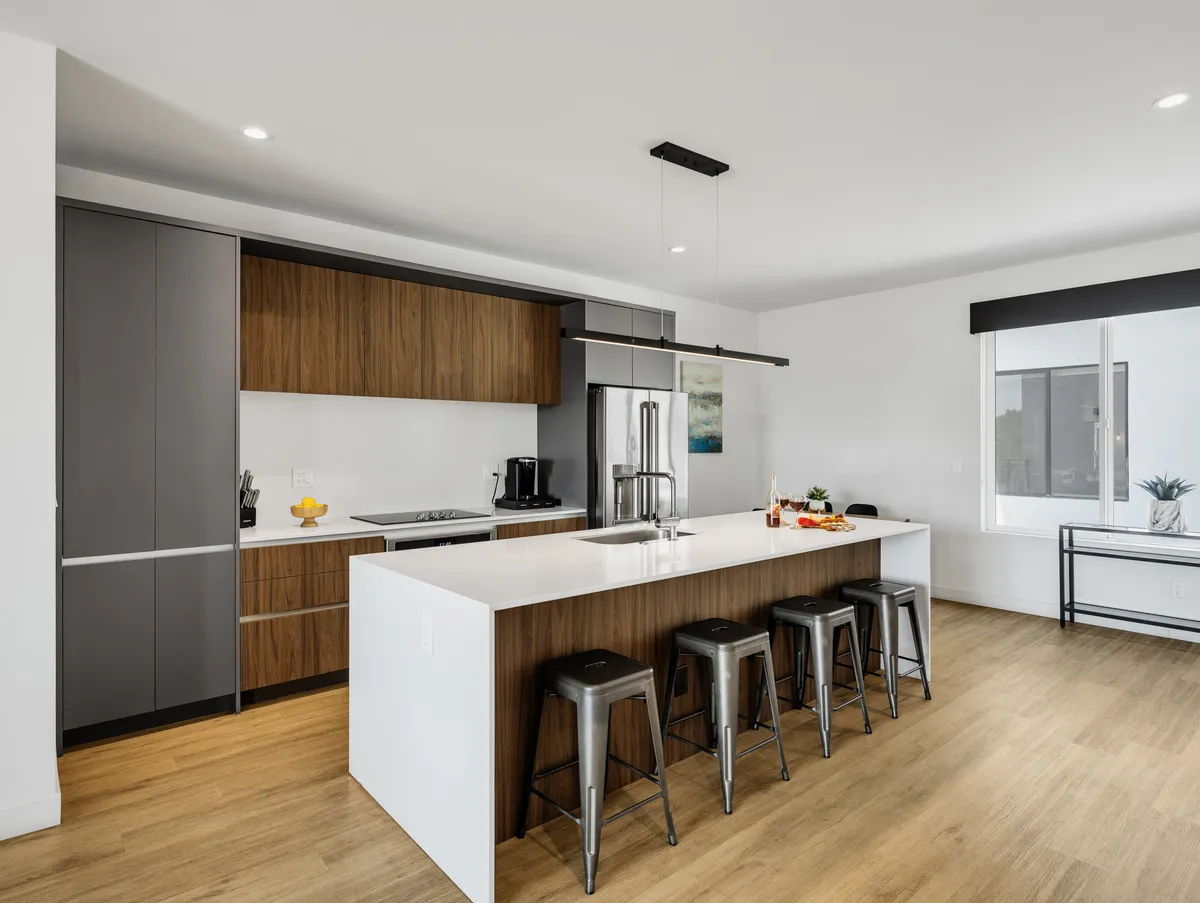 A bright, open-concept kitchen with a spacious island and bar stools, modern cabinetry, and high-end appliances. The layout invites gathering and socializing, with plenty of workspace and seating for group meals or casual snacks.