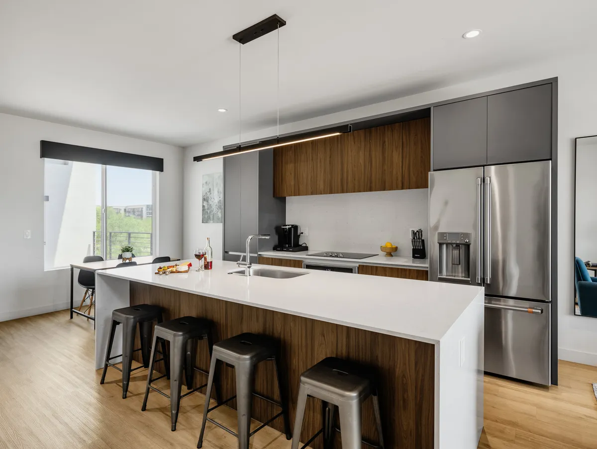 A bright, contemporary kitchen with an island countertop, bar stools, modern appliances, and a window view. The space feels open and functional, ideal for preparing meals or gathering with friends and family.