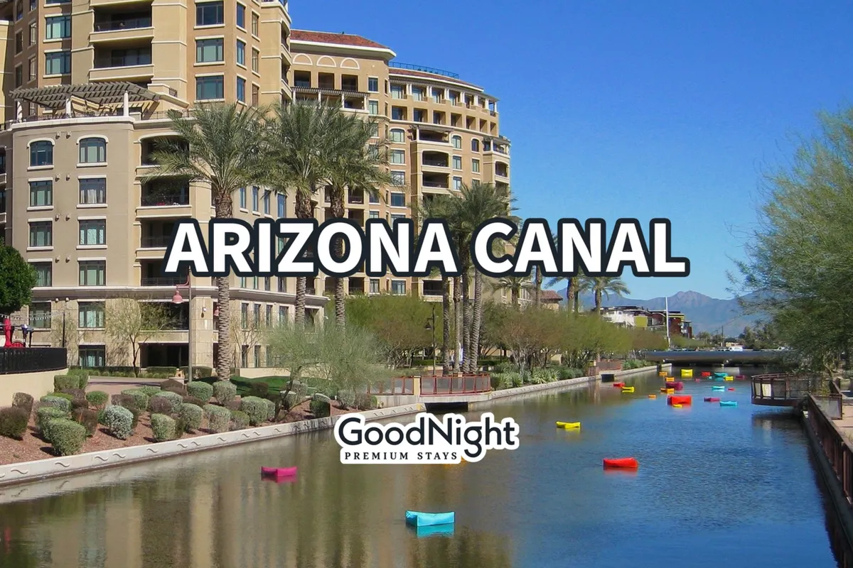 A vibrant view of the Arizona Canal lined with colorful boats, modern buildings, and palm trees, suggesting a lively urban area perfect for walking, boating, and waterfront dining. The festive atmosphere hints at local events and energetic outdoor life.