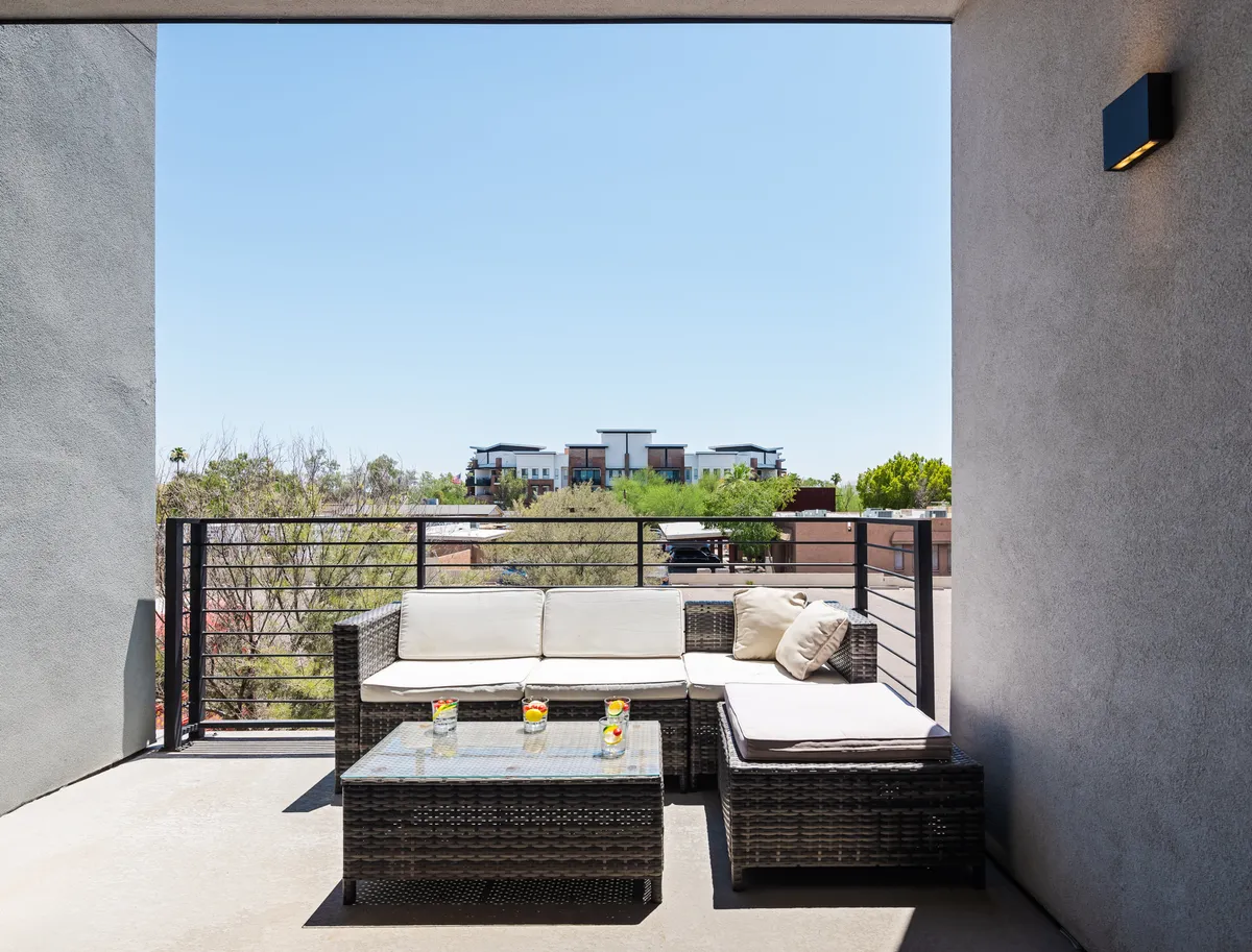 An outdoor patio with a stylish wicker seating arrangement and a glass-top table, set against a scenic view of the surrounding landscape. The space is designed for casual gatherings, quiet relaxation, or enjoying a morning coffee in a serene setting.